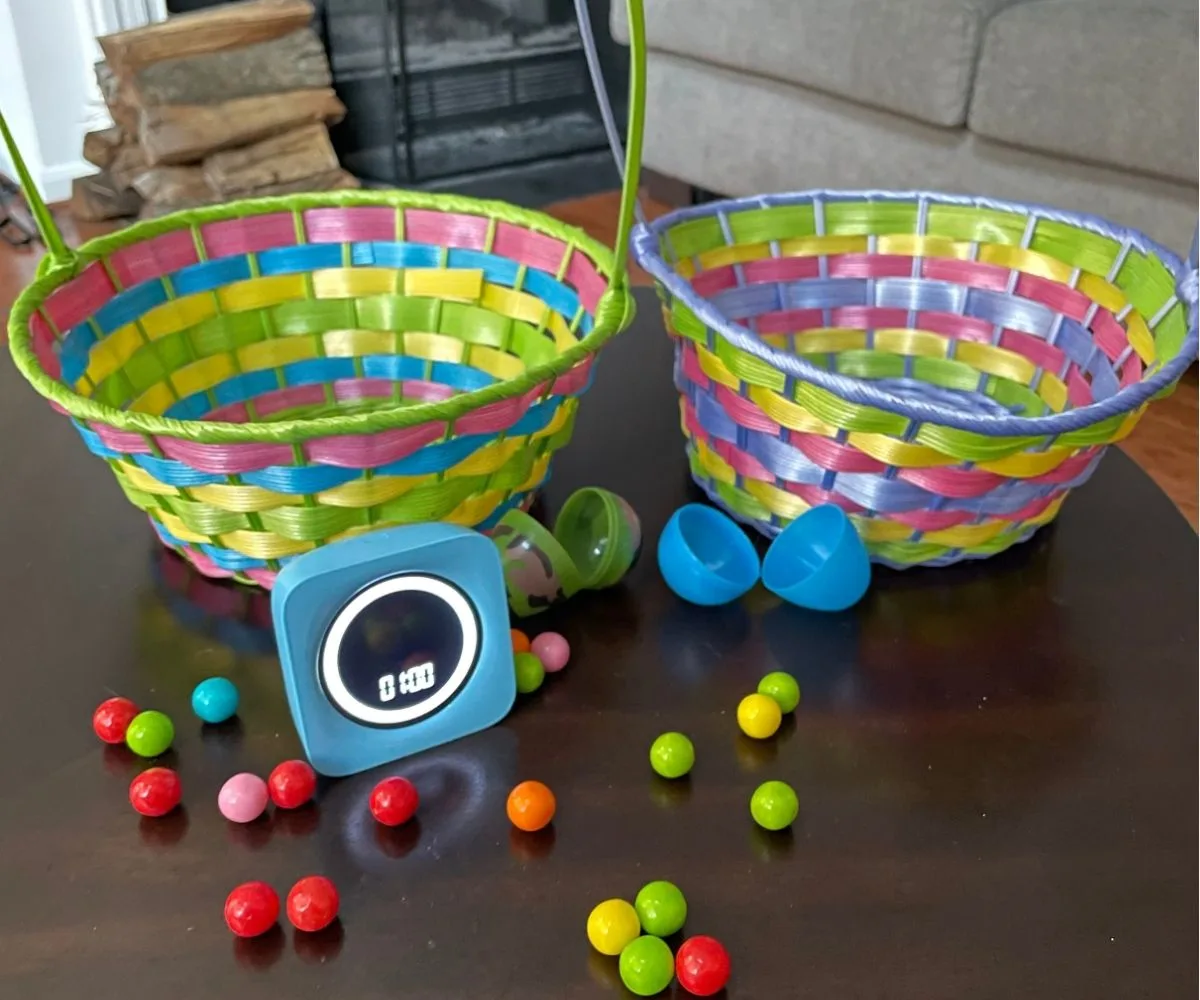 two Easter egg baskets with scattered colorful gumballs, one-minute timer, and two opened, empty Easter eggs