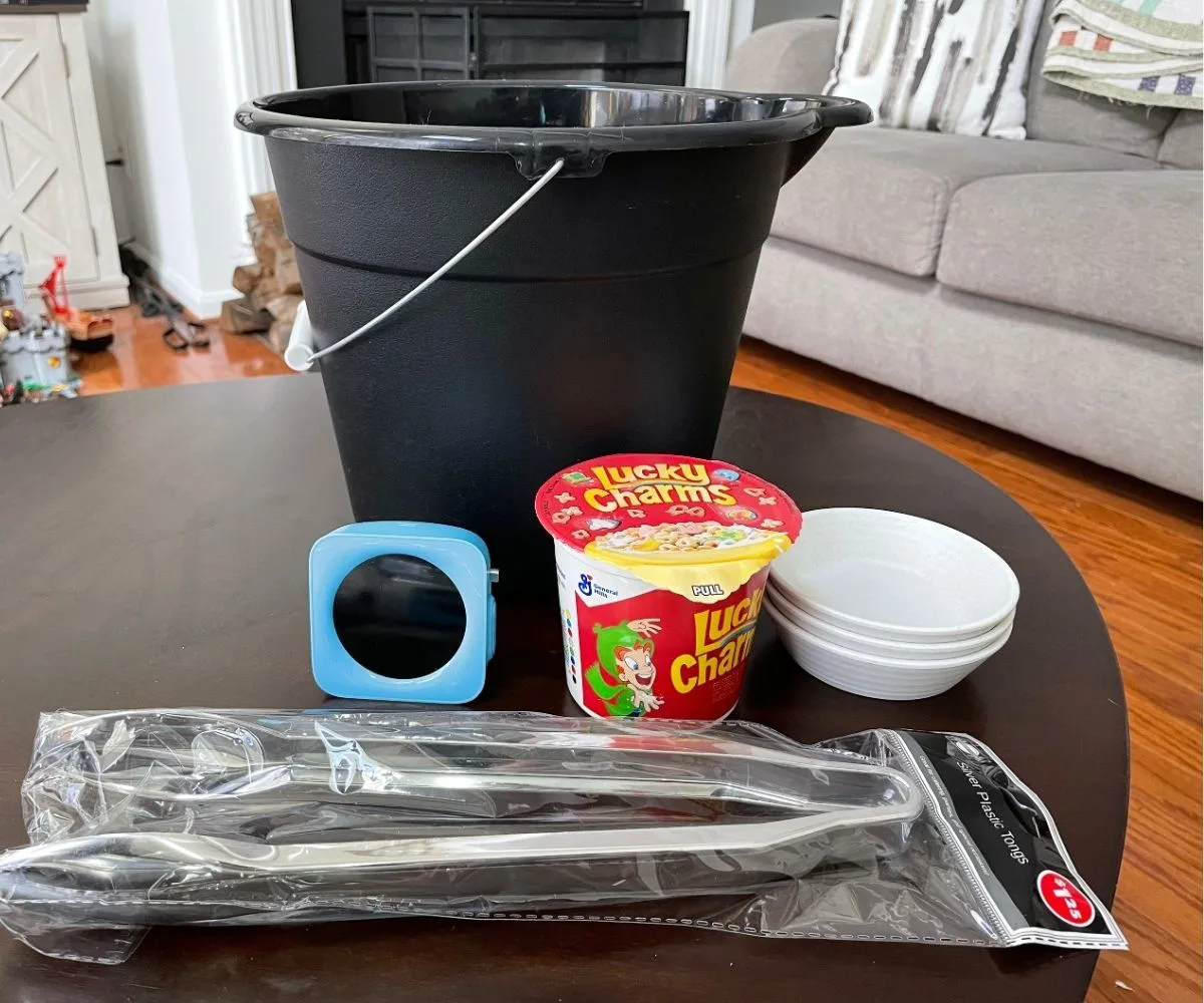 black bucket, timer, Lucky Charms container, three smaller containers, and silver tongs