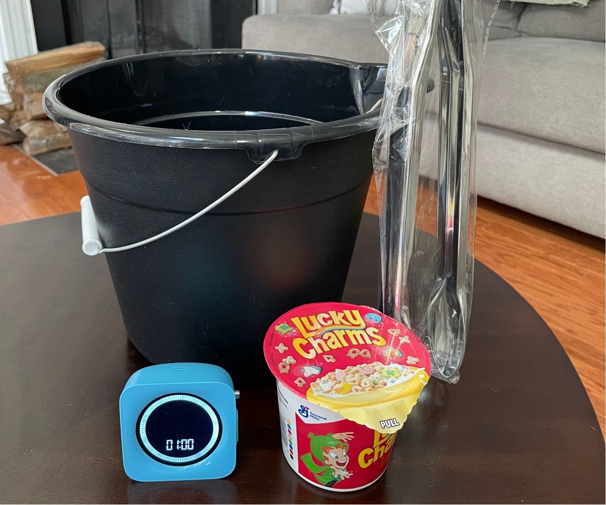 timer at 1 minute, black bucket, silver tongs, and small container of Lucky Charms cereal