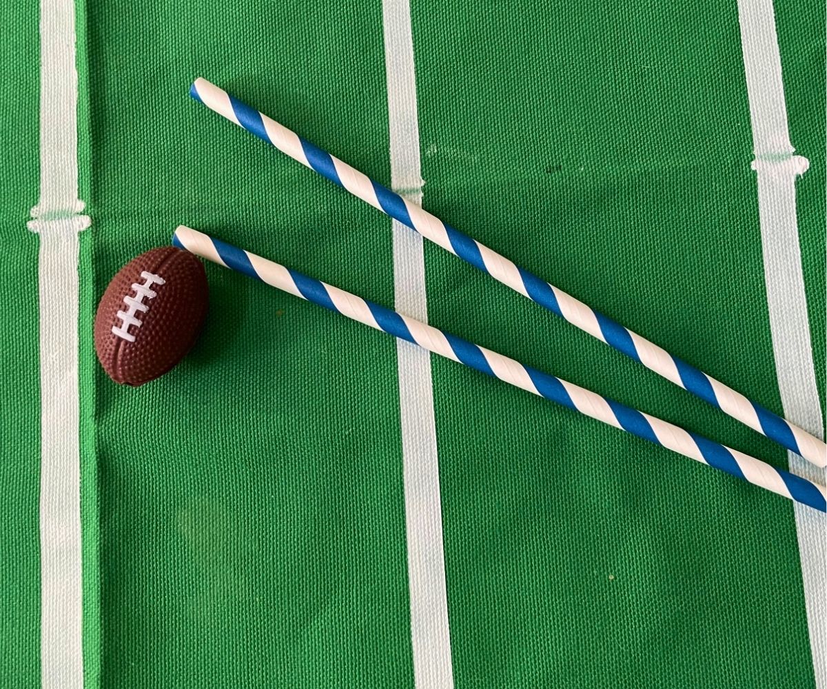 two colorful straws next to toy football on green and white tablecloth