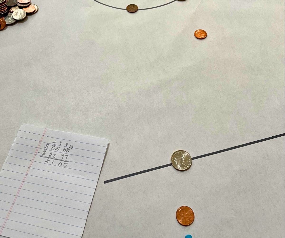 pencil pushing coins into the center circle, with money math on paper