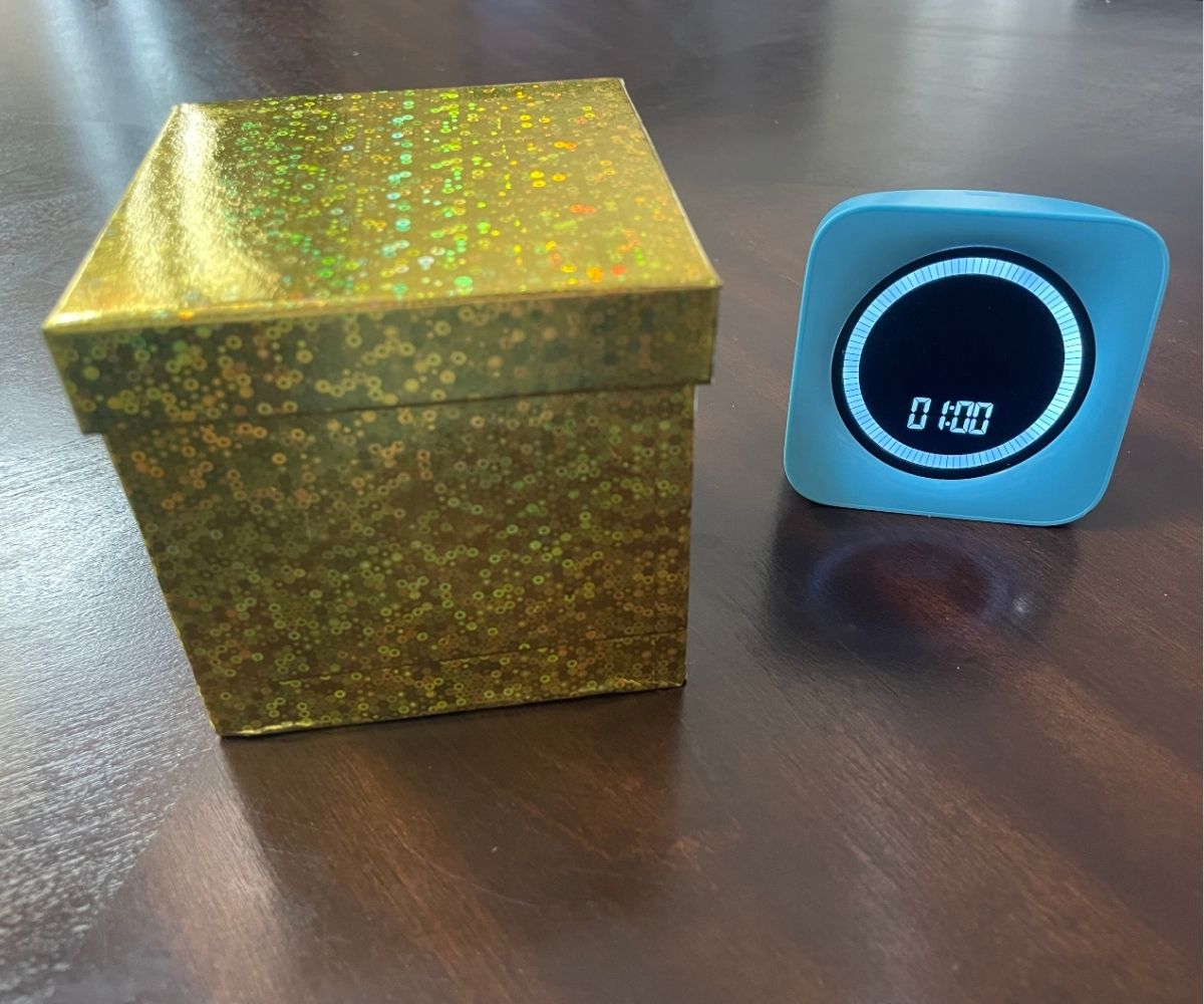 sparkly small gold box filled with coins next to pale blue timer