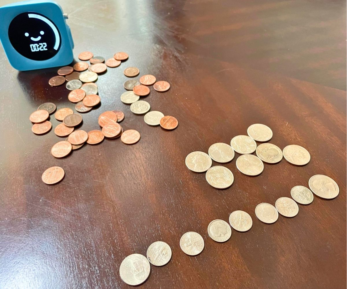 timer with 22 seconds remaining, next to big pile of coins and two rows with various coins equaling $1.00 each