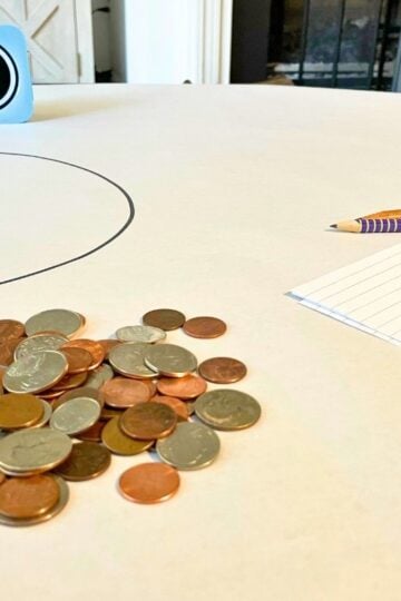 large white sheet of paper, timer, big pile of coins, pencils, scratch paper, and big circle in center
