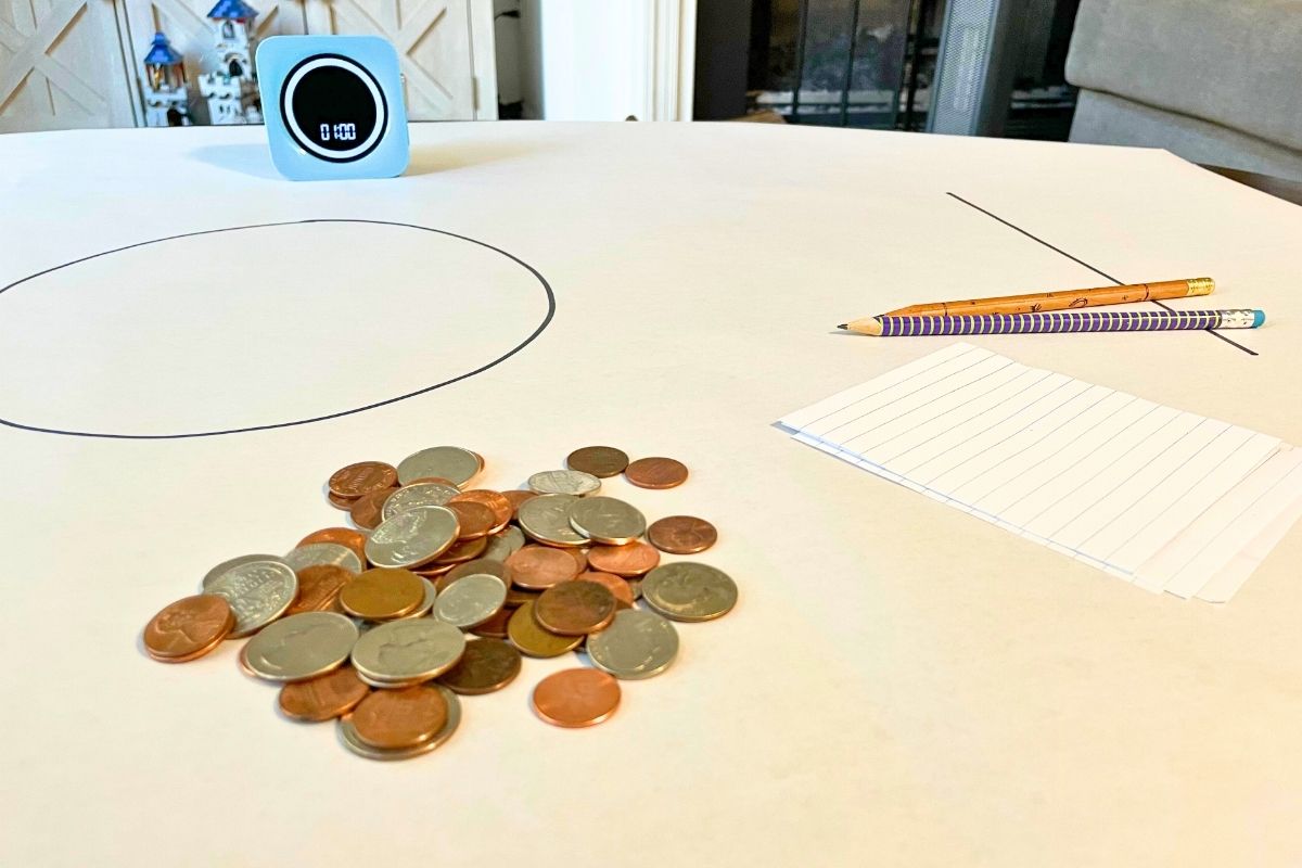 large white sheet of paper, timer, big pile of coins, pencils, scratch paper, and big circle in center