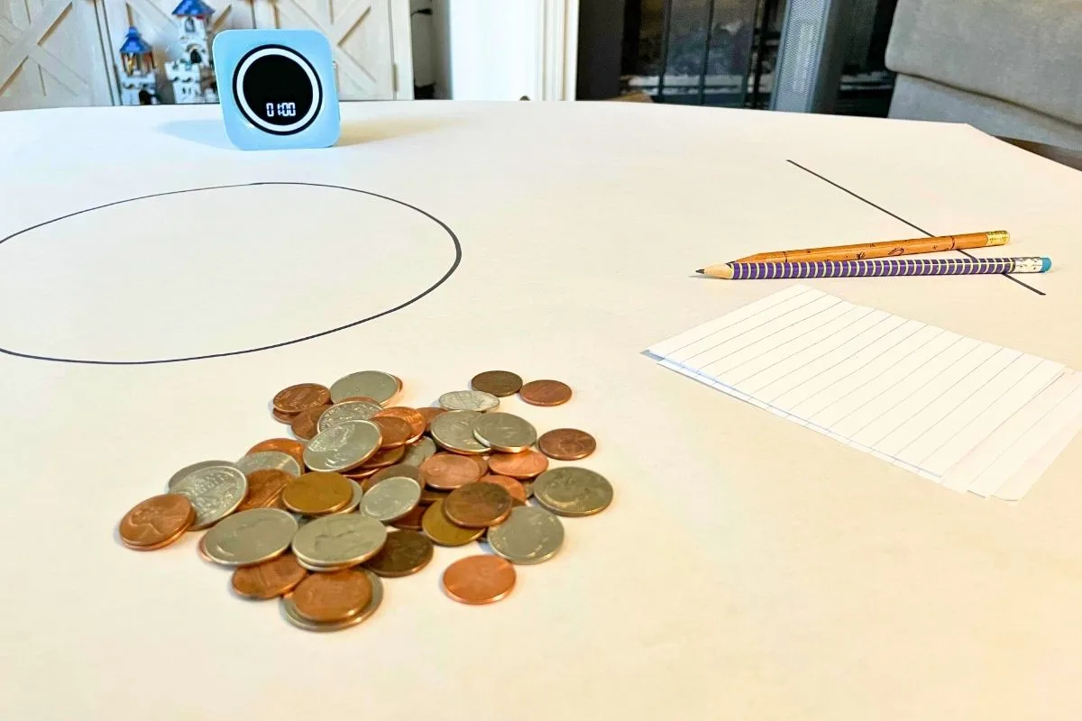 large white sheet of paper, timer, big pile of coins, pencils, scratch paper, and big circle in center