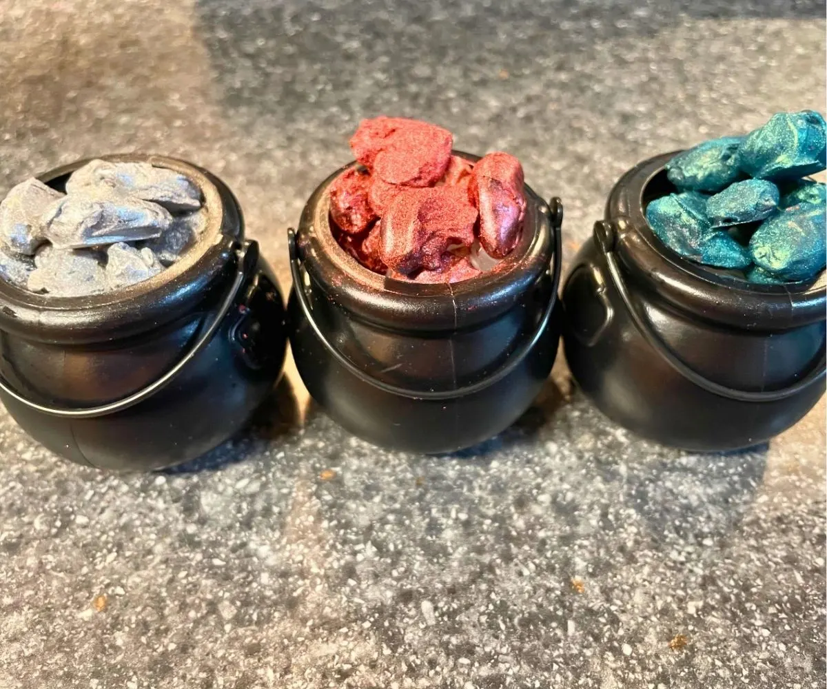 small black cauldrons filled with different colored candy coated and glimmery almonds