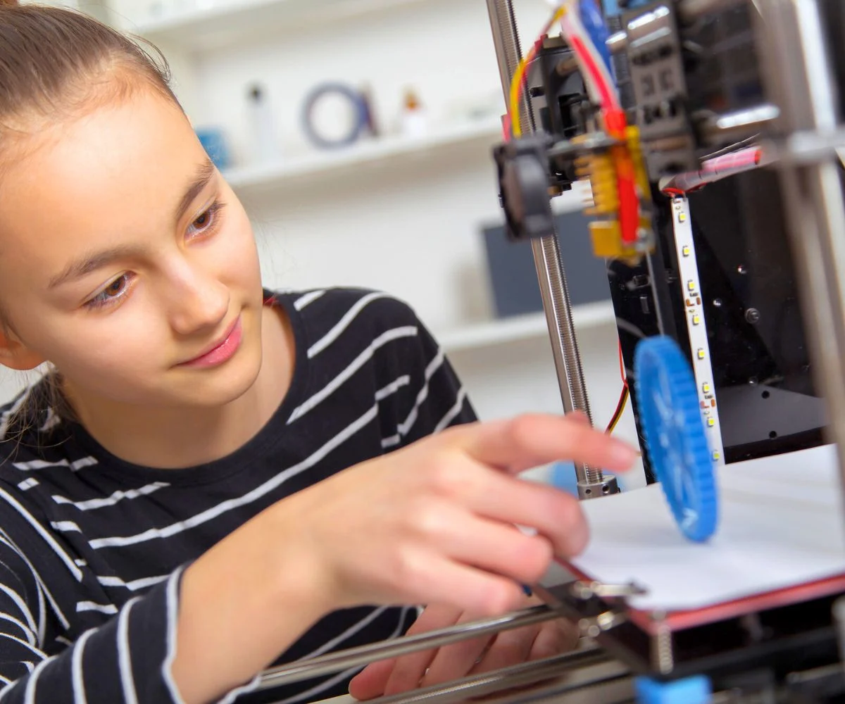 high school girl in striped shirt at 3D printer working on prototype