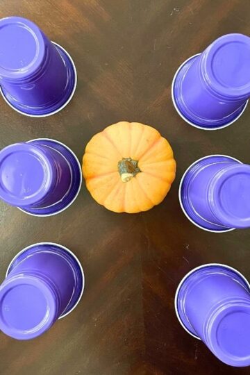 three rows of dark purple cups upside down with mini pumpkin on table