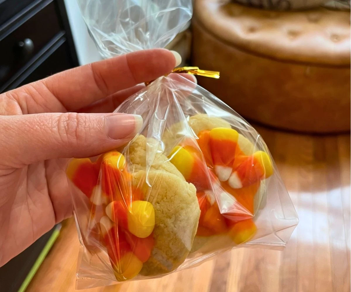 woman holding two candy corn coated cookies in plastic bag