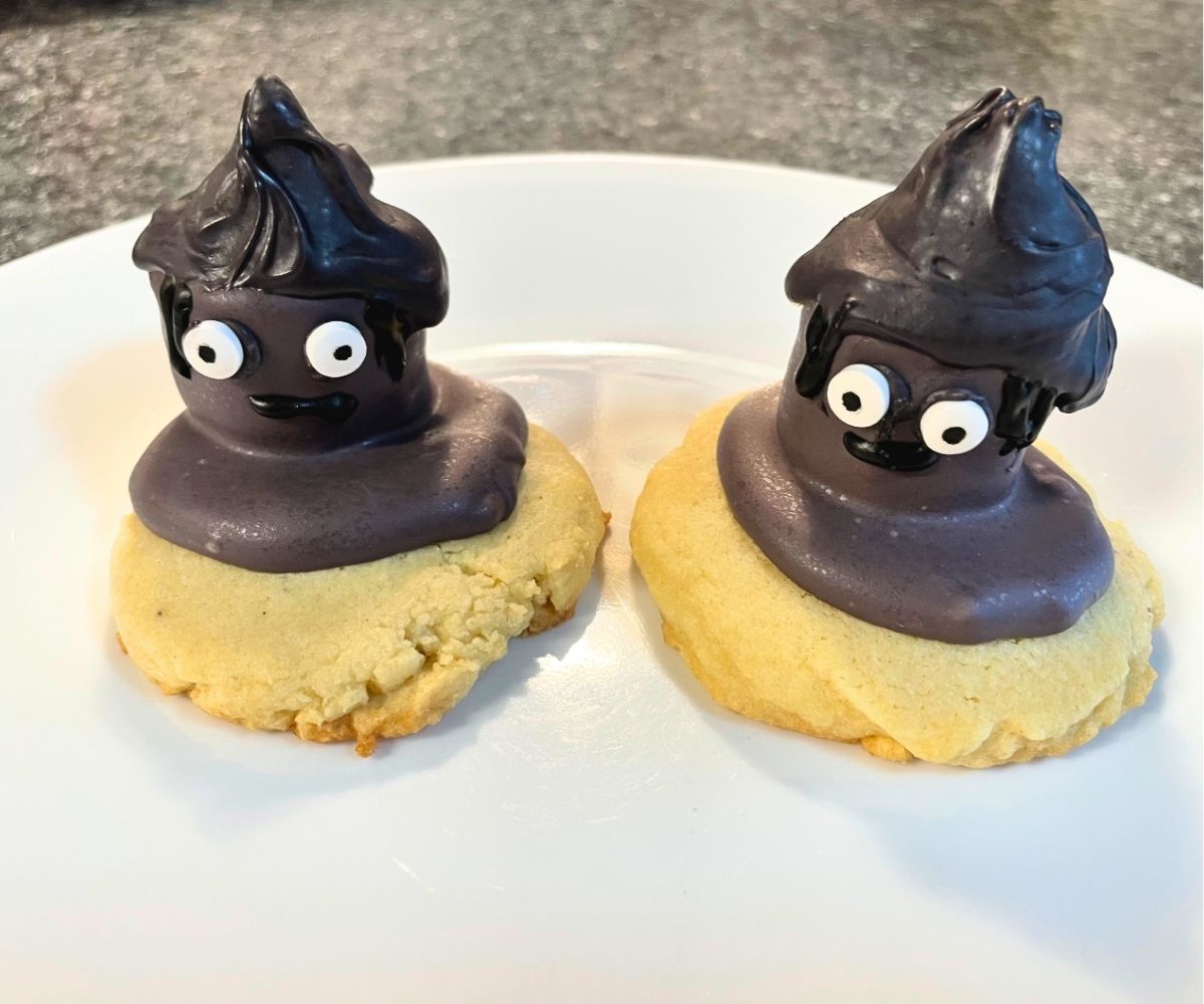 two sugar cookies topped with purple dipped marshmallows, puddle of purple, and the marshmallows have eyes and a black hat