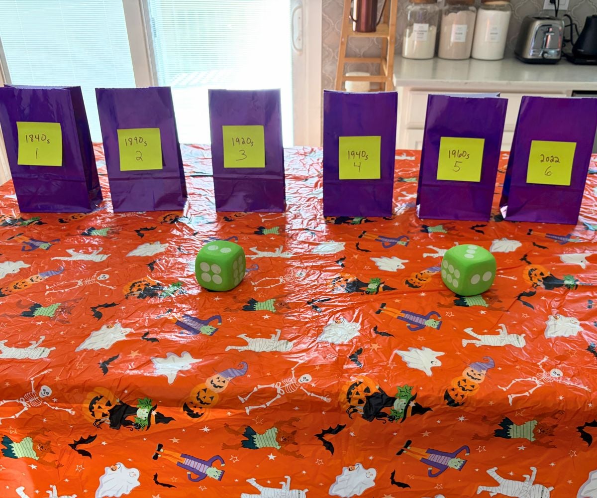 Orange Halloween tablecloth with six purple bags with Post-It Notes and two large green dice