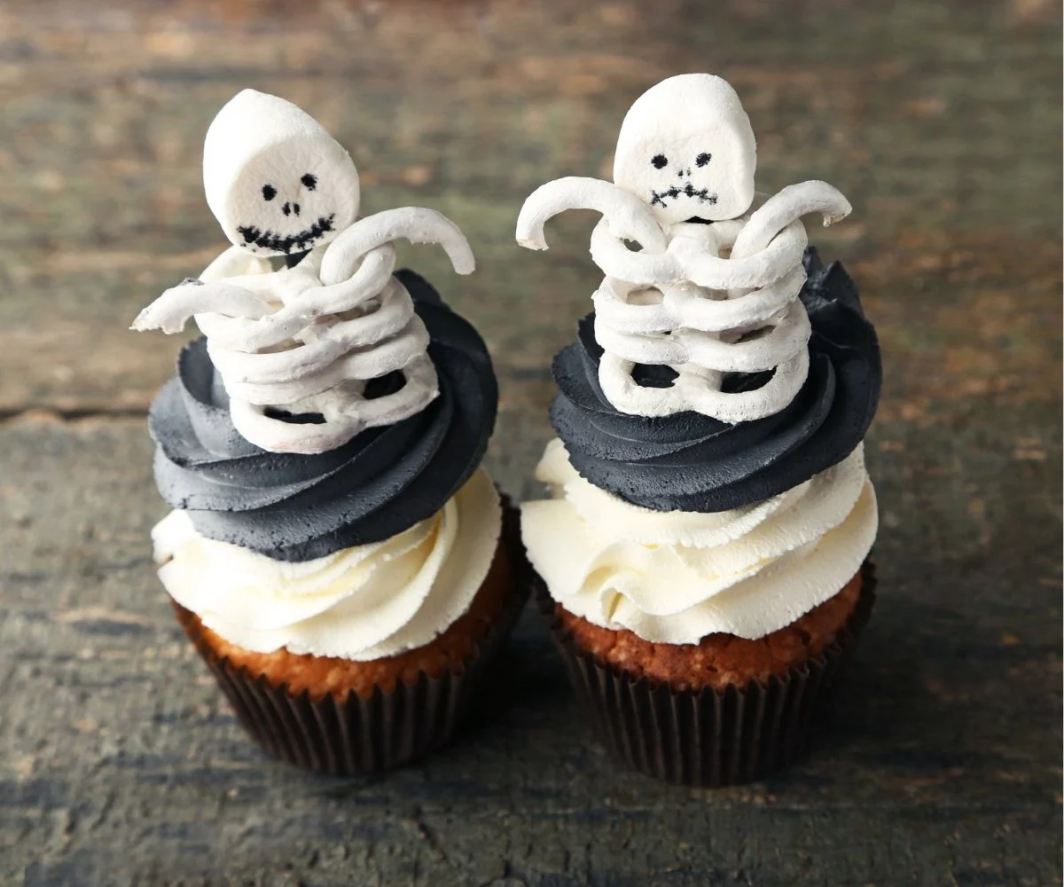 two cupcakes with white and black icing, and a pile of white pretzels and a marshmallow on top of each