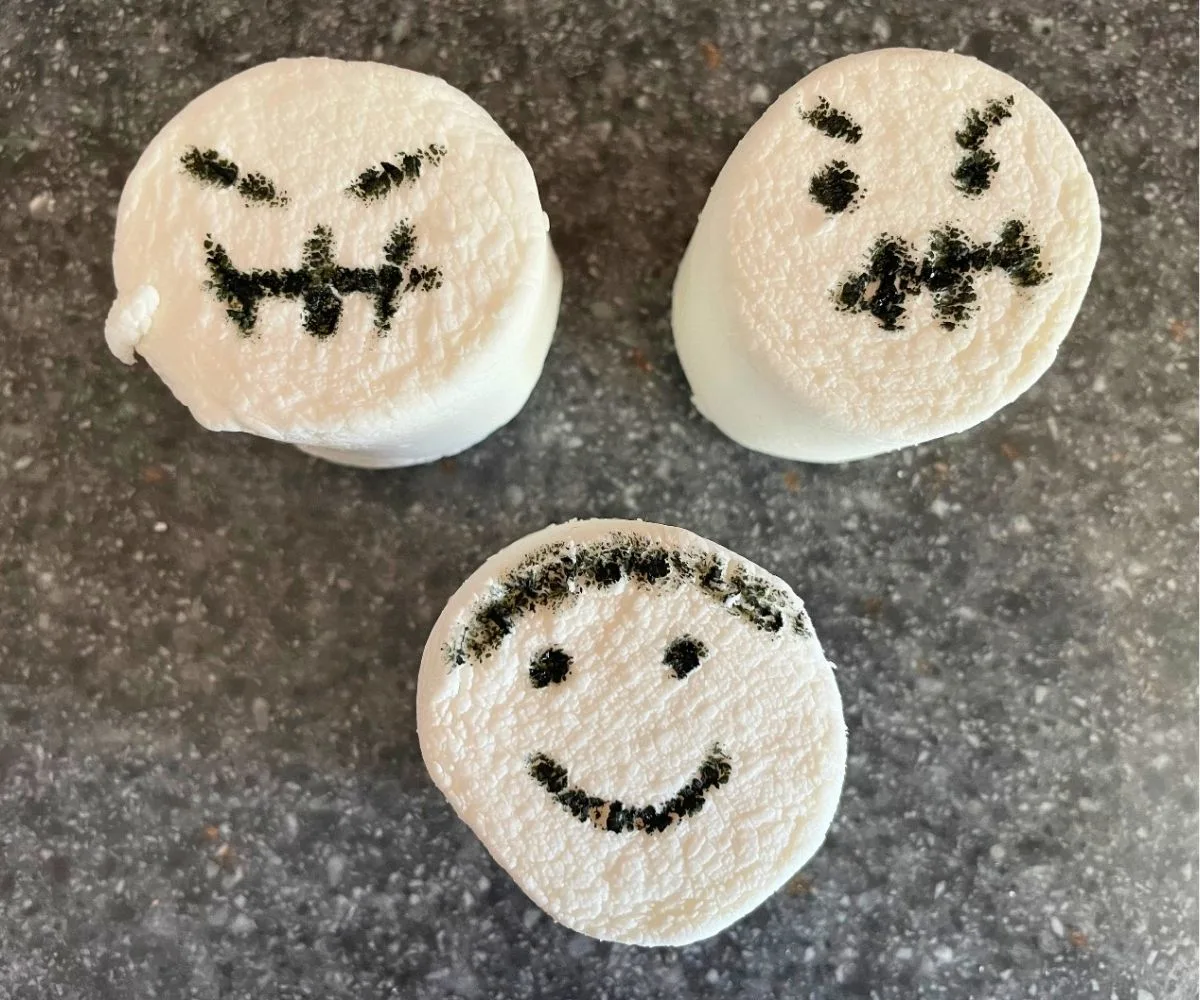 three large marshmallows on kitchen counter with spooky faces written on in edible marker
