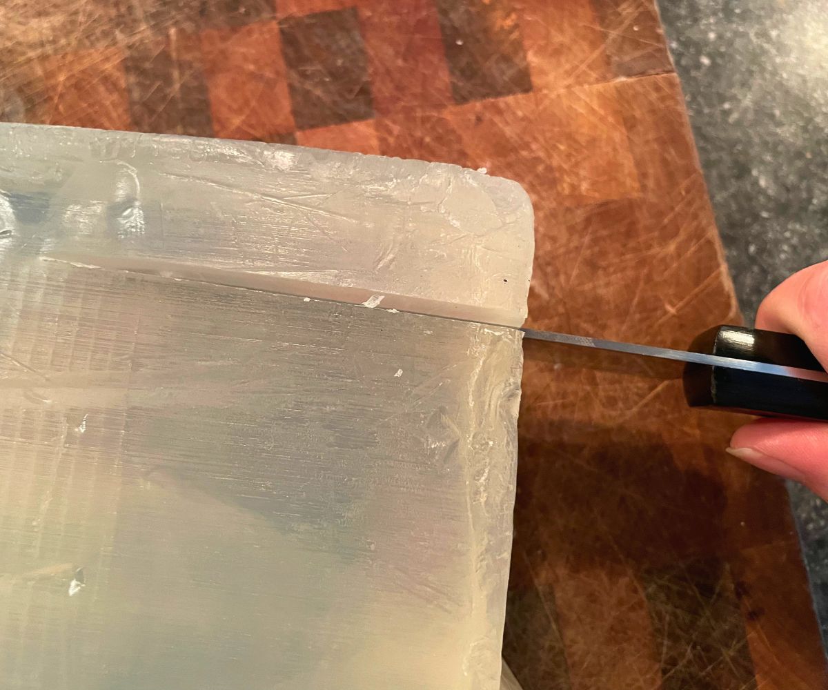 woman cutting soap base on cutting board