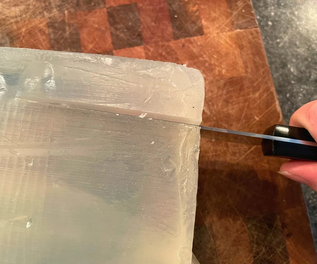woman cutting soap base on cutting board