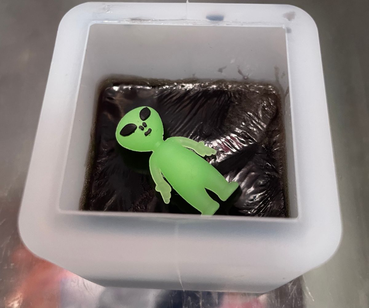 cube filled halfway with black soap and an alien toy on the top