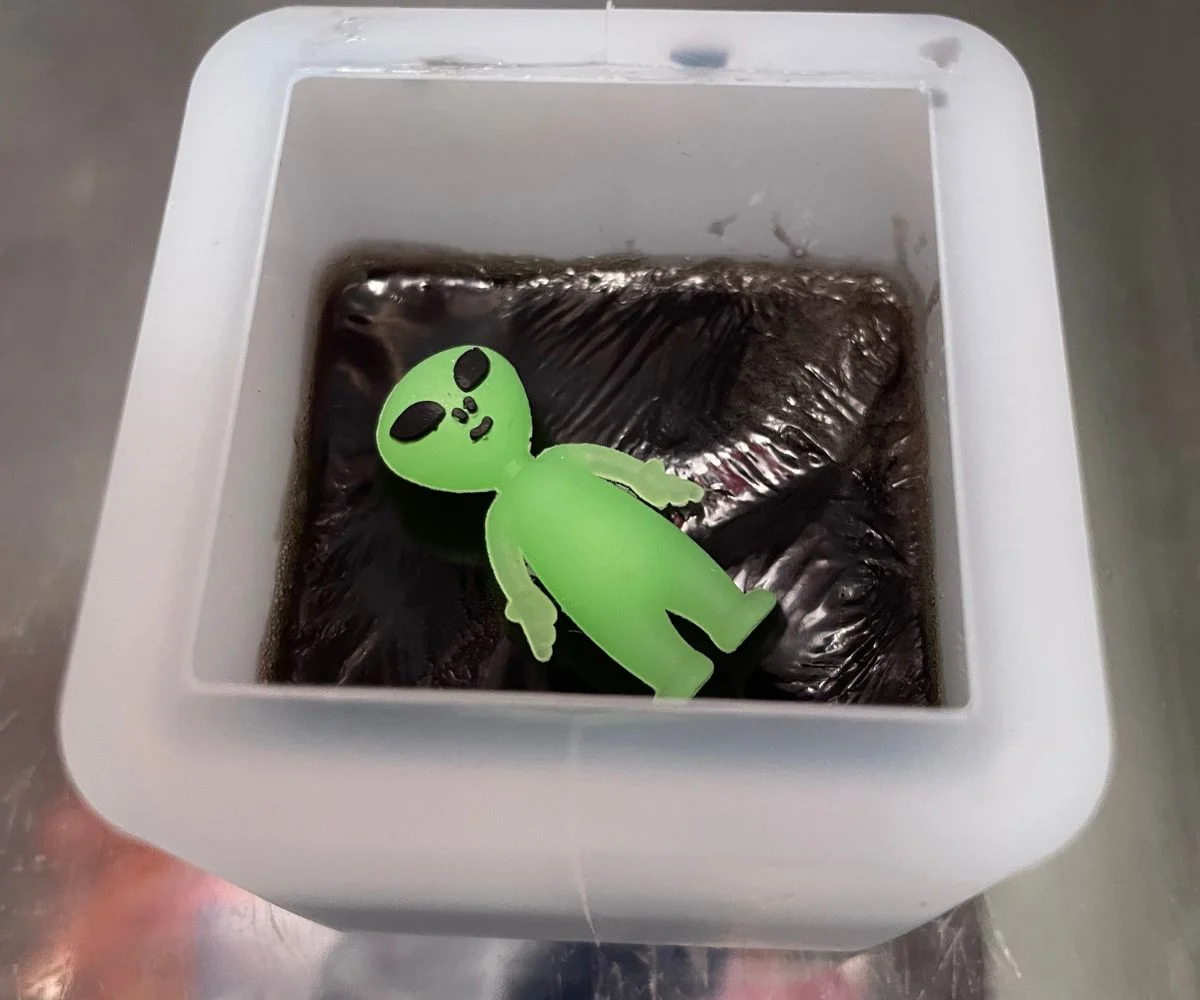 cube filled halfway with black soap and an alien toy on the top