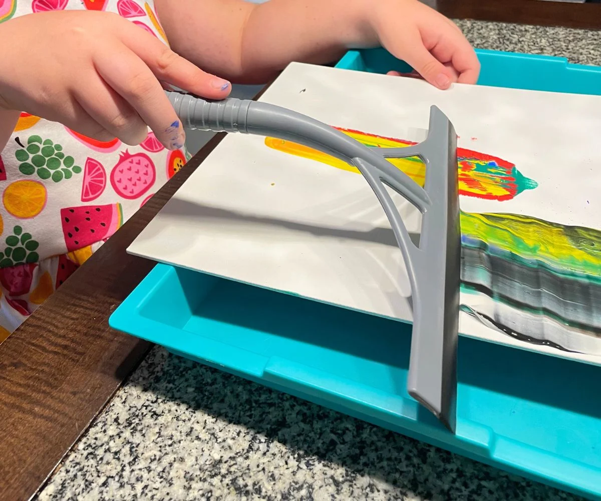 girl with squeegee and globs of different colored paints on canvas