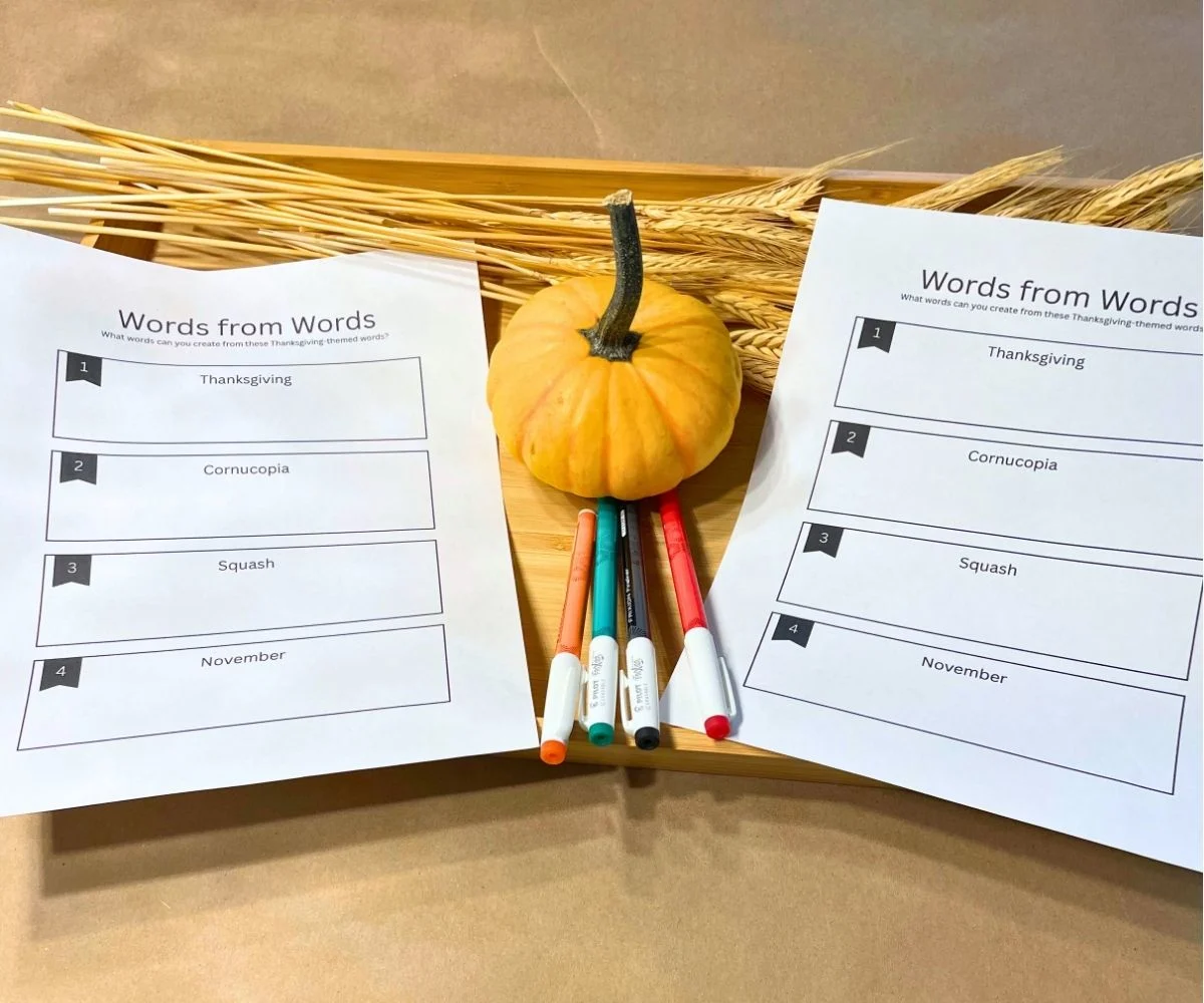 two printable words from words game on light wooden tray with mini pumpkin, wheat, and set of markers