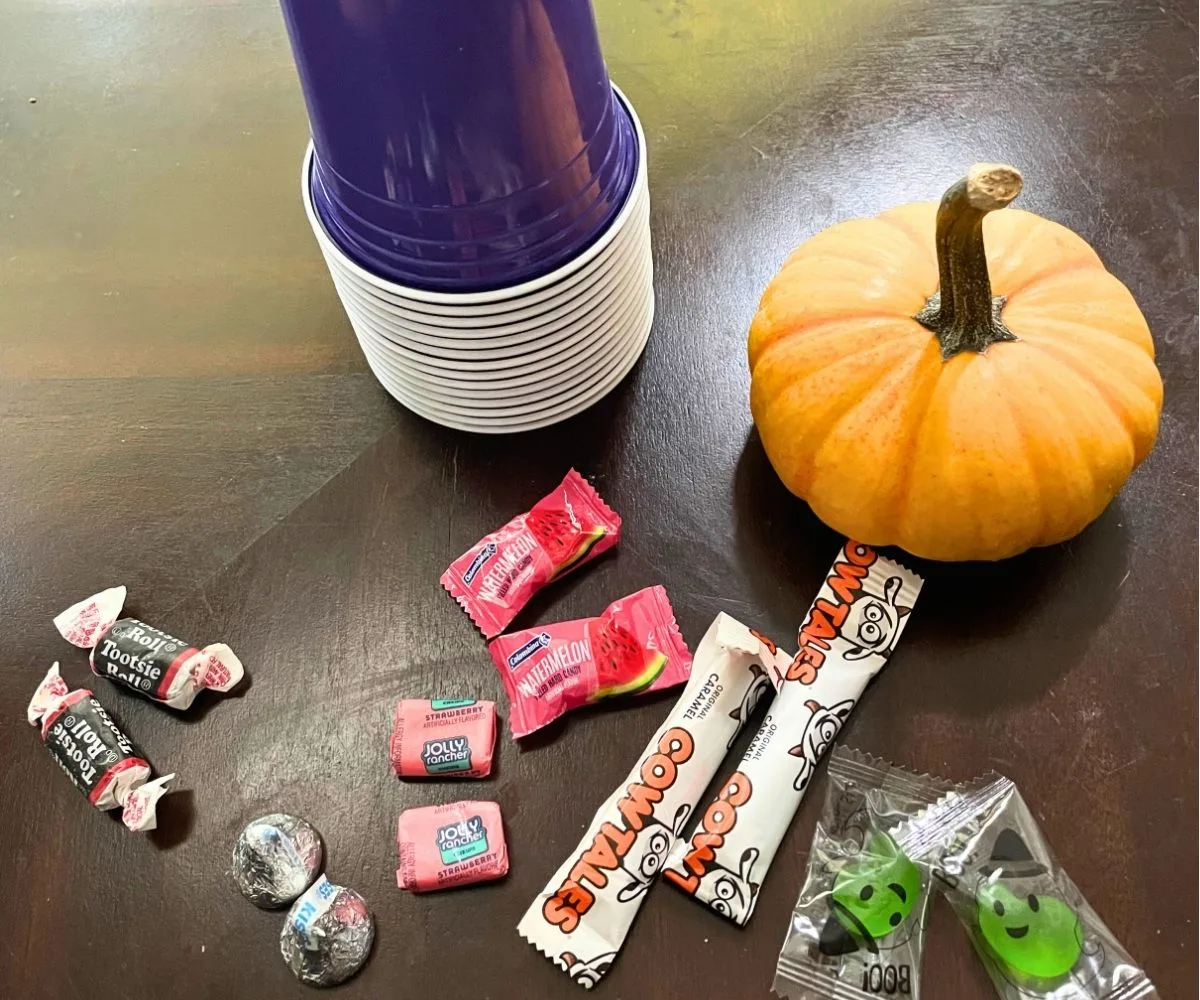 stack of dark purple cups with little pumpkin next to pile of paired up candies