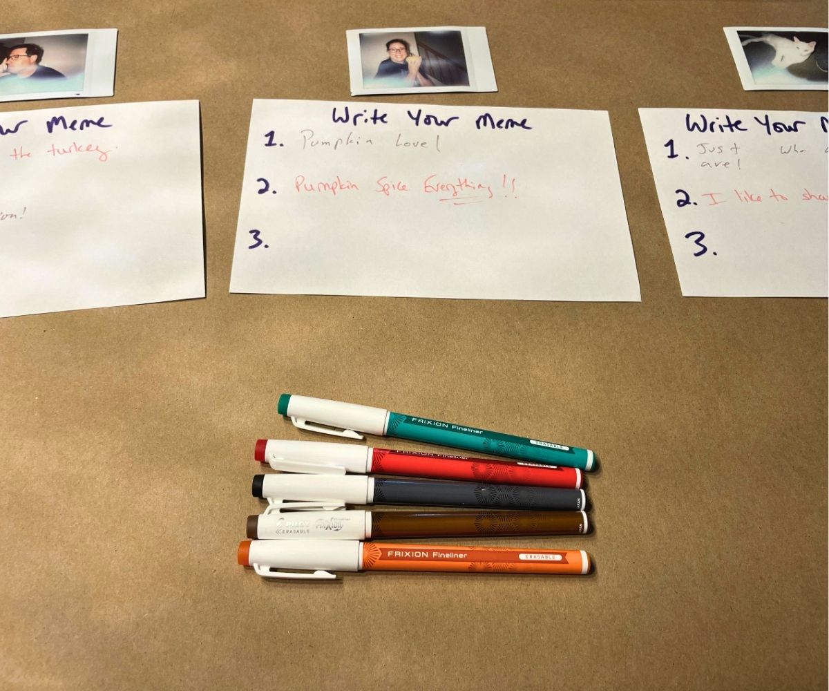 three instant photos of guests with three index cards for memes and markers laid out
