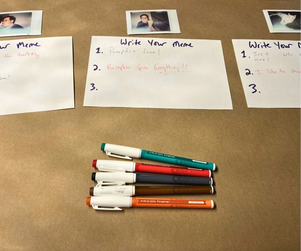 three instant photos of guests with three index cards for memes and markers laid out