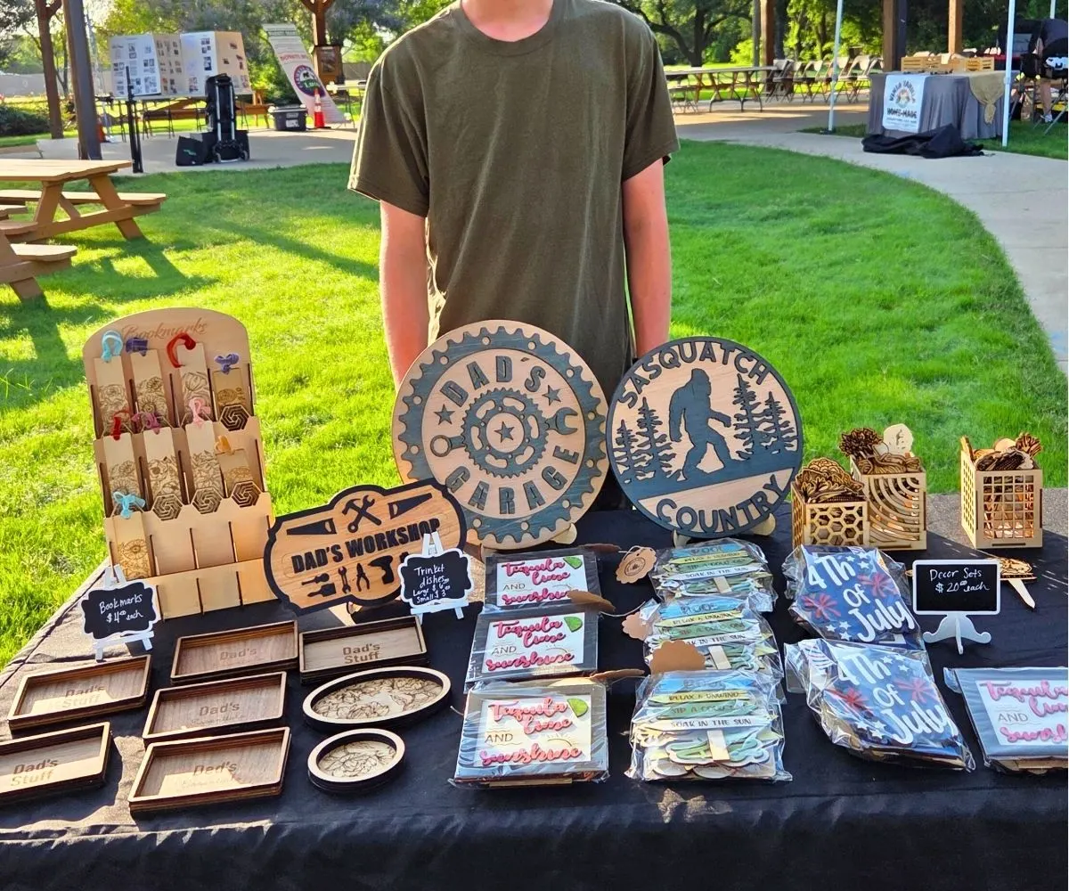 Asher standing behind his table of lots of CO2 laser printing products at a farmer's market