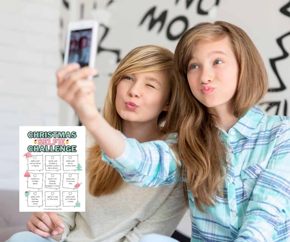 two teen girls taking a selfie with a PDF of the Christmas selfie challenge