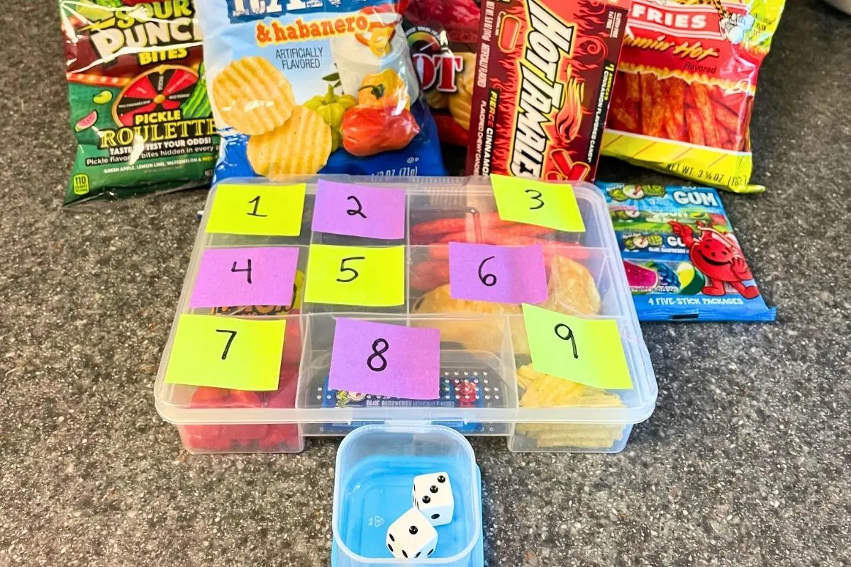 tacklebox with colored and numbered post its on outside, in front of dice and lots of extreme flavored snacks