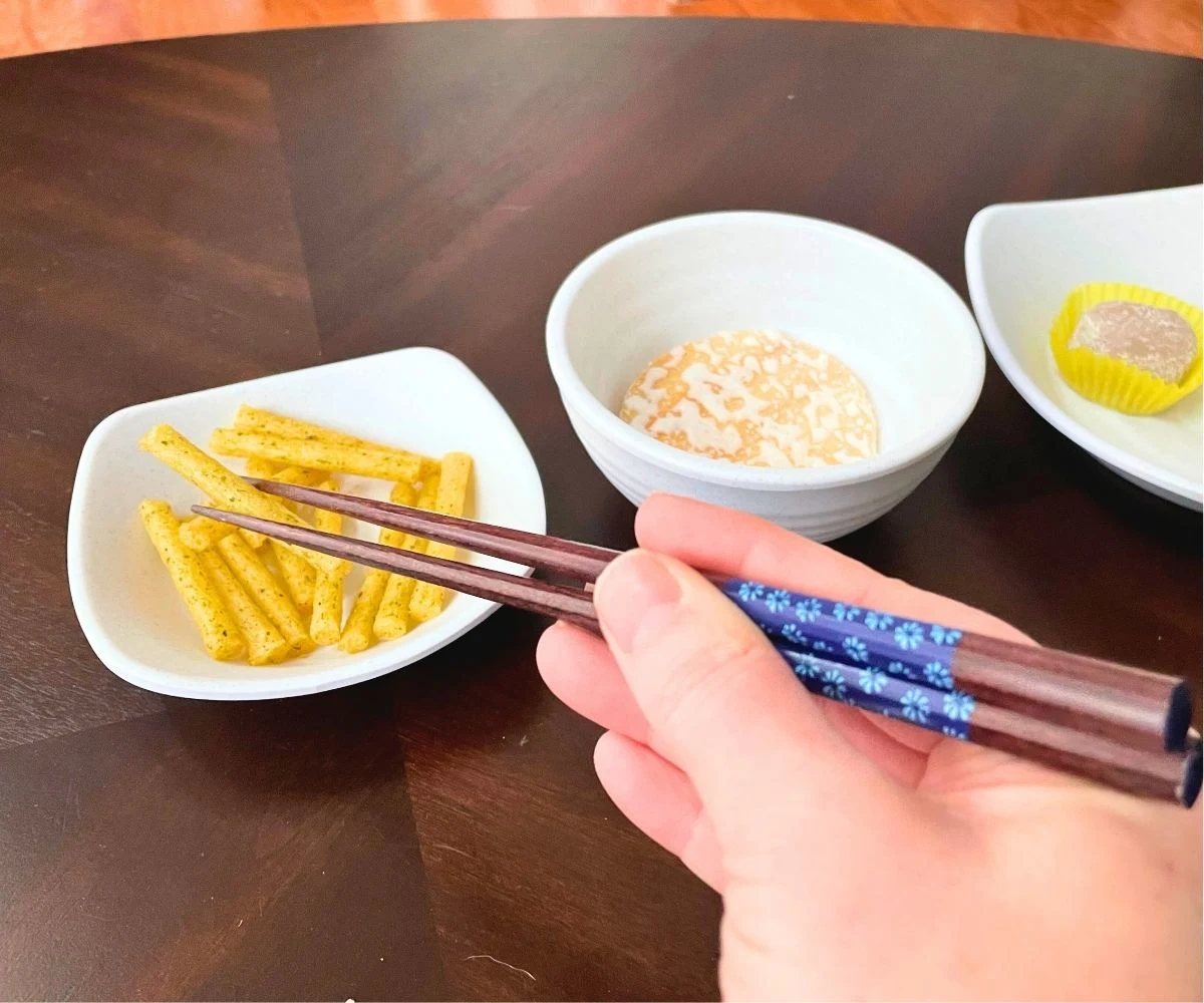 teen using chopsticks with three different bowls of different snacks