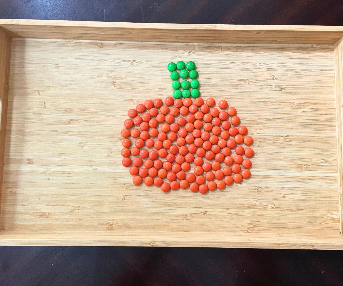 light wooden tray with M&M art in shape of pumpkin