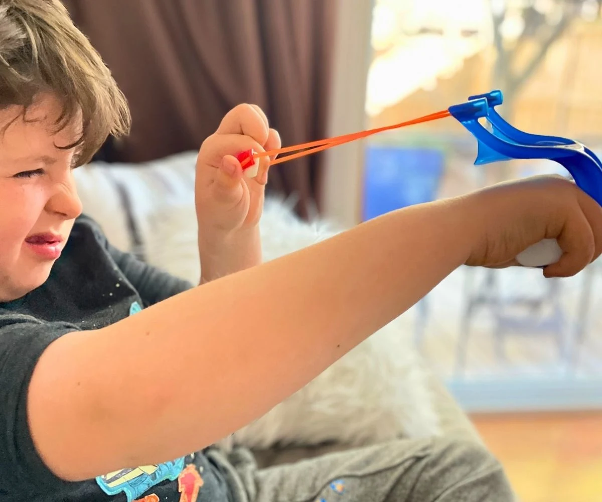boy kid with eye pinched closed, ready to fling marshmallow in marshmallow sling