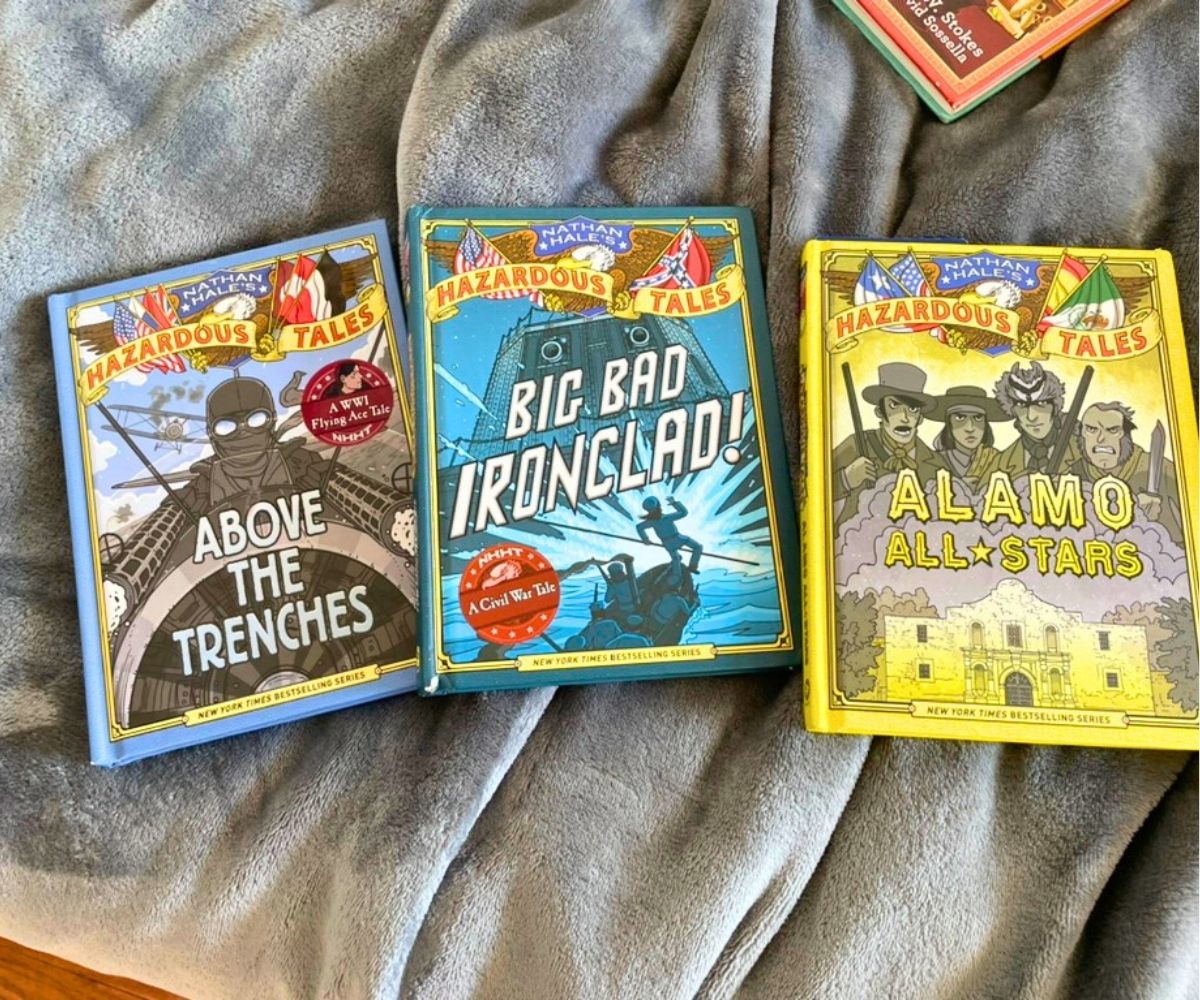 three colorful historical graphic novels for tweens on gray blanket on bed