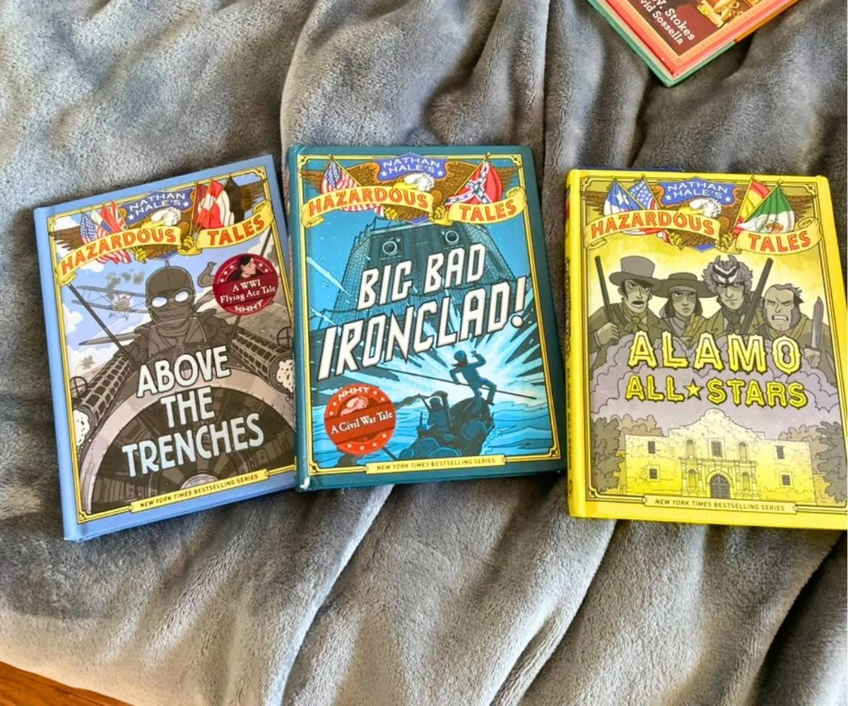 three colorful historical graphic novels for tweens on gray blanket on bed