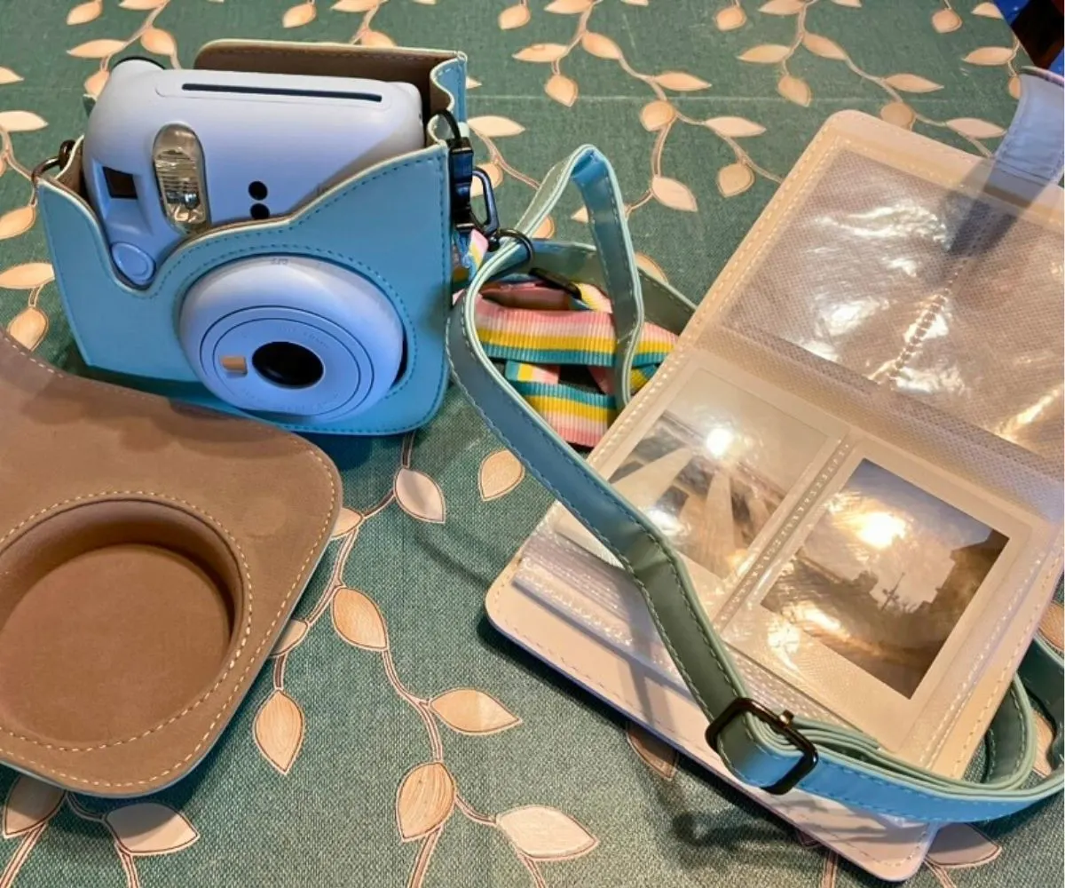 pale blue Instant camera on a kitchen table opened to an album filled with photos