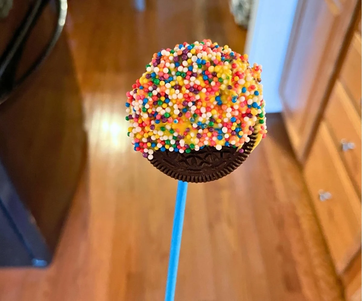 finished Oreo on blue lollipop stick in rainbow covered sprinkles dish