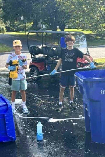 Splash Brothers outside with cleaning supplies next to two blue garbage cans they've cleaned