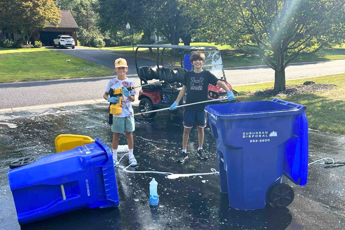 Splash Brothers outside with cleaning supplies next to two blue garbage cans they've cleaned