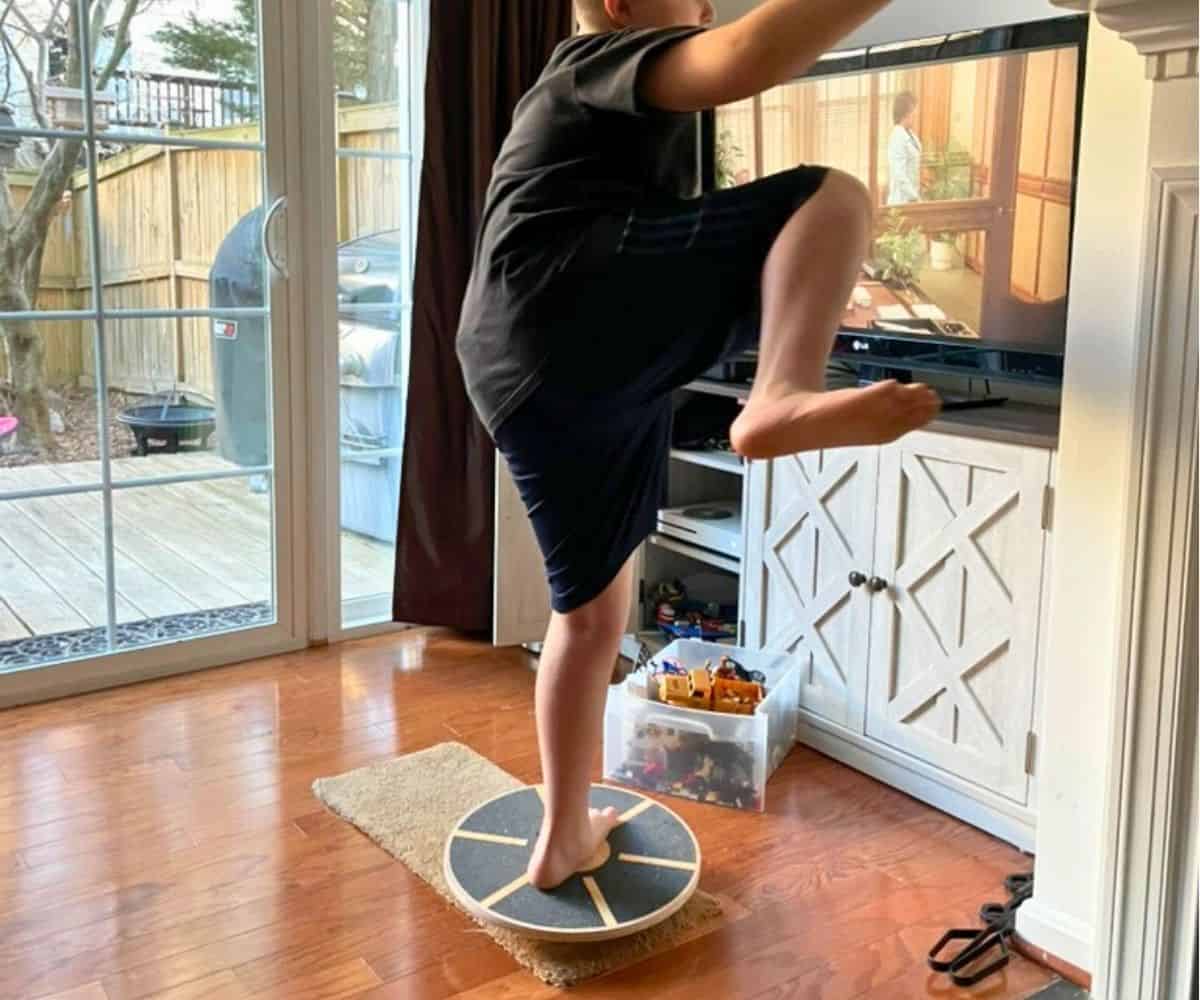 preteen boy with one leg up in air and the other balanced on the balance board in front of tv