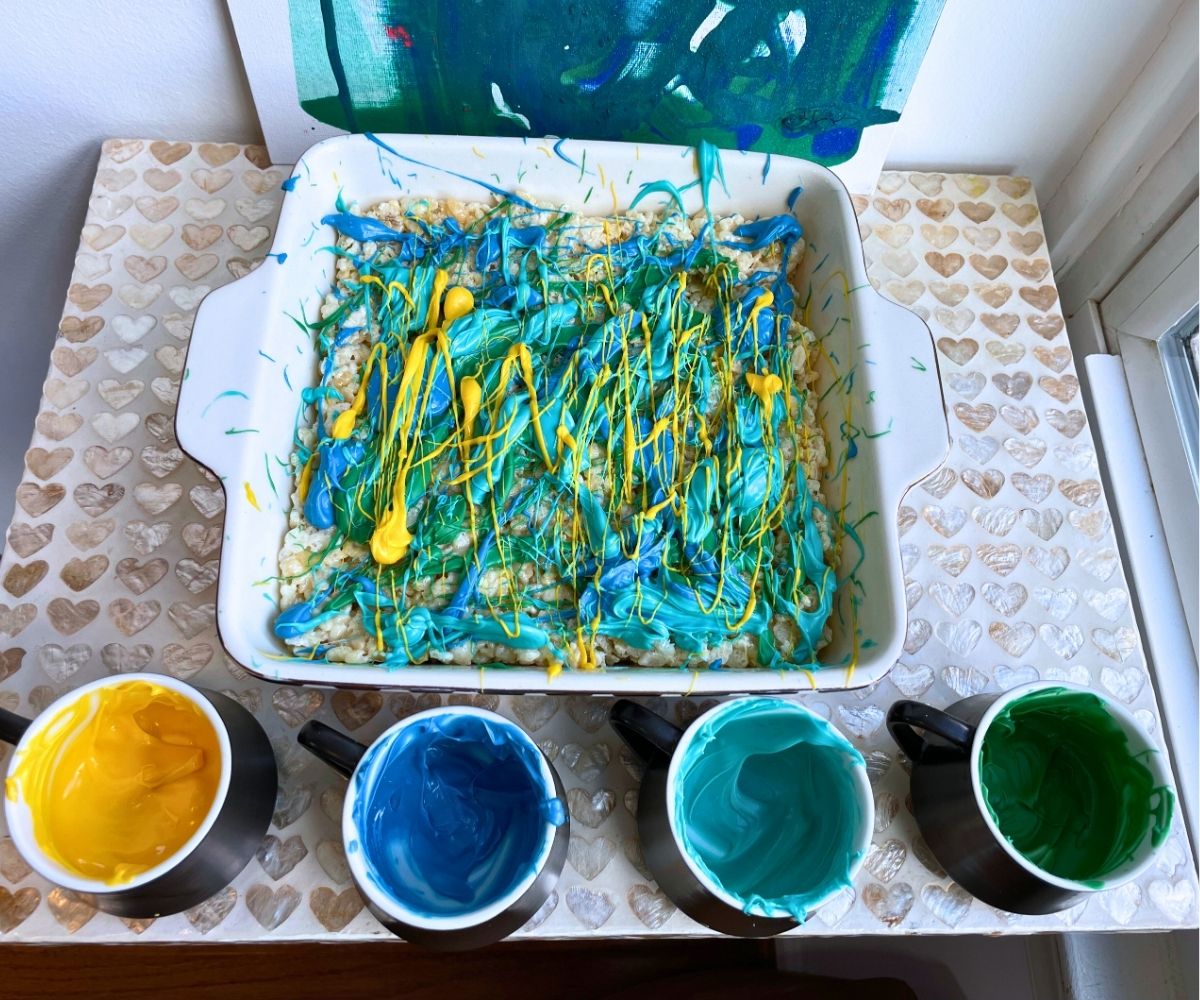 pan of graffiti candy melts-covered Rice krispies treats with four mini cups of melted candy melts next to it