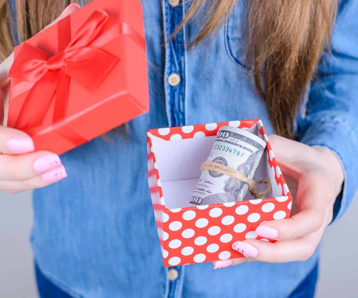 teen girl opening up a bright, small red box with money inside