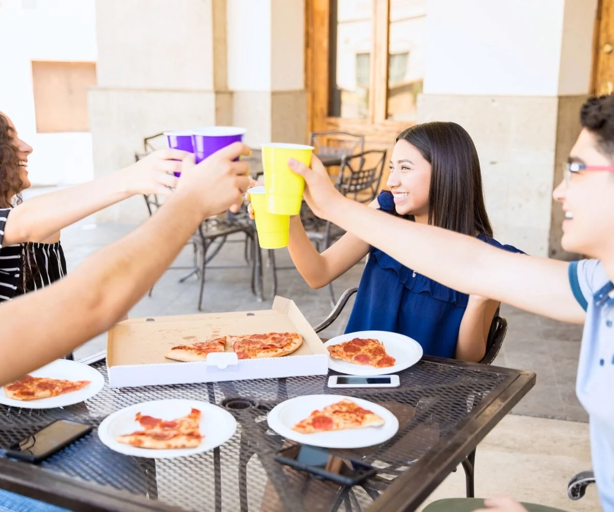Group of four teens around pizza out at a restaurant, smiling