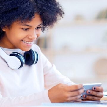 teen girl with headphones, smiling at phone, earning cash online