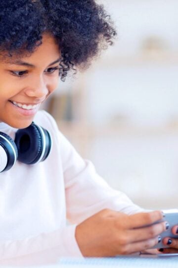 teen girl with headphones, smiling at phone, earning cash online
