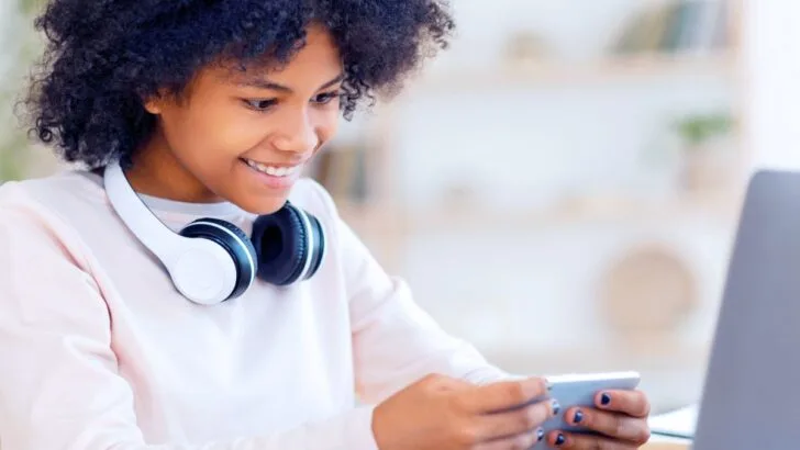 teen girl with headphones, smiling at phone, earning cash online