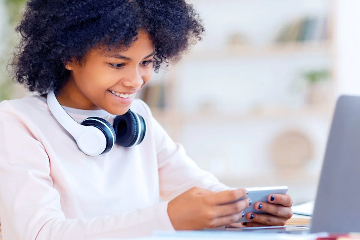 teen girl with headphones, smiling at phone, earning cash online