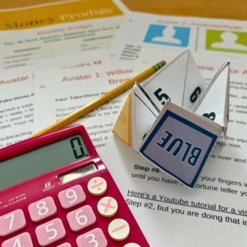 printed out fortune teller and money game on light wooden table with pink calculator
