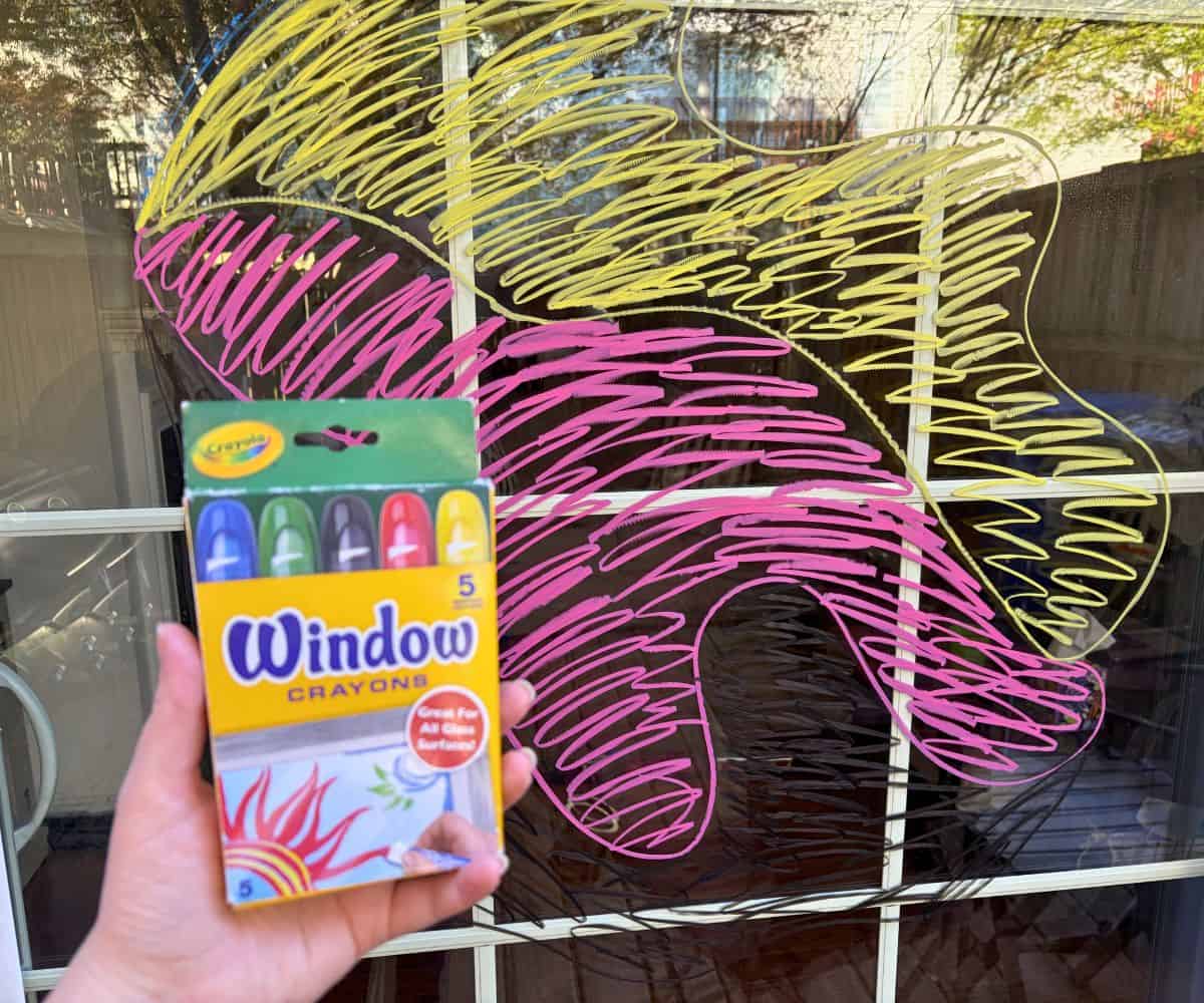 silly mural on patio door, with hand holding up box of Window crayons used for it