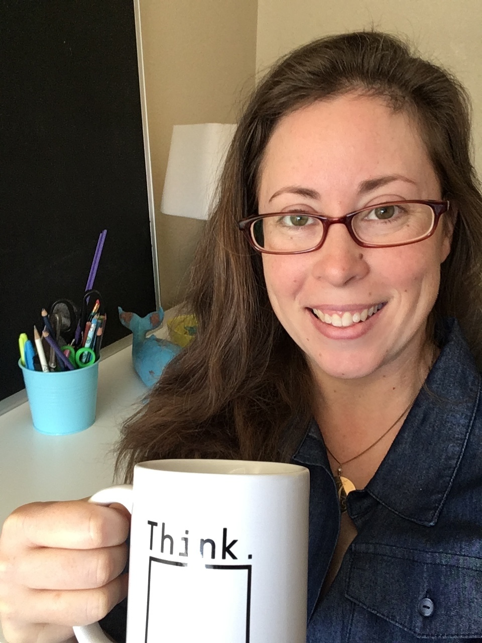 Amanda L Grossman money educator wearing jean shirt and with a mug that says Think over a box